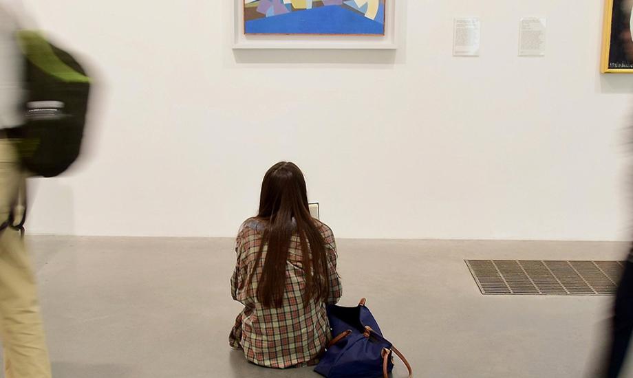 People at an exhibition. One girl sitting down and looking at picture.